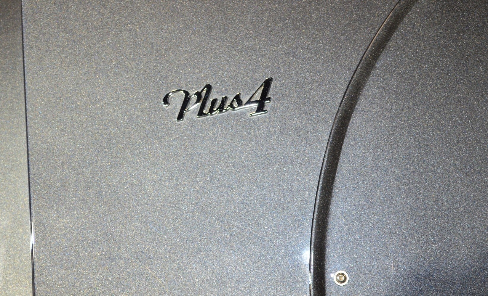Close-up of a stylized Plus 4 emblem on a metallic car surface