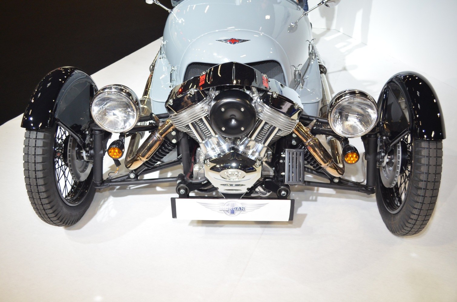 Exposed V-twin engine with round headlights and spoked wheels on a three-wheeler front.