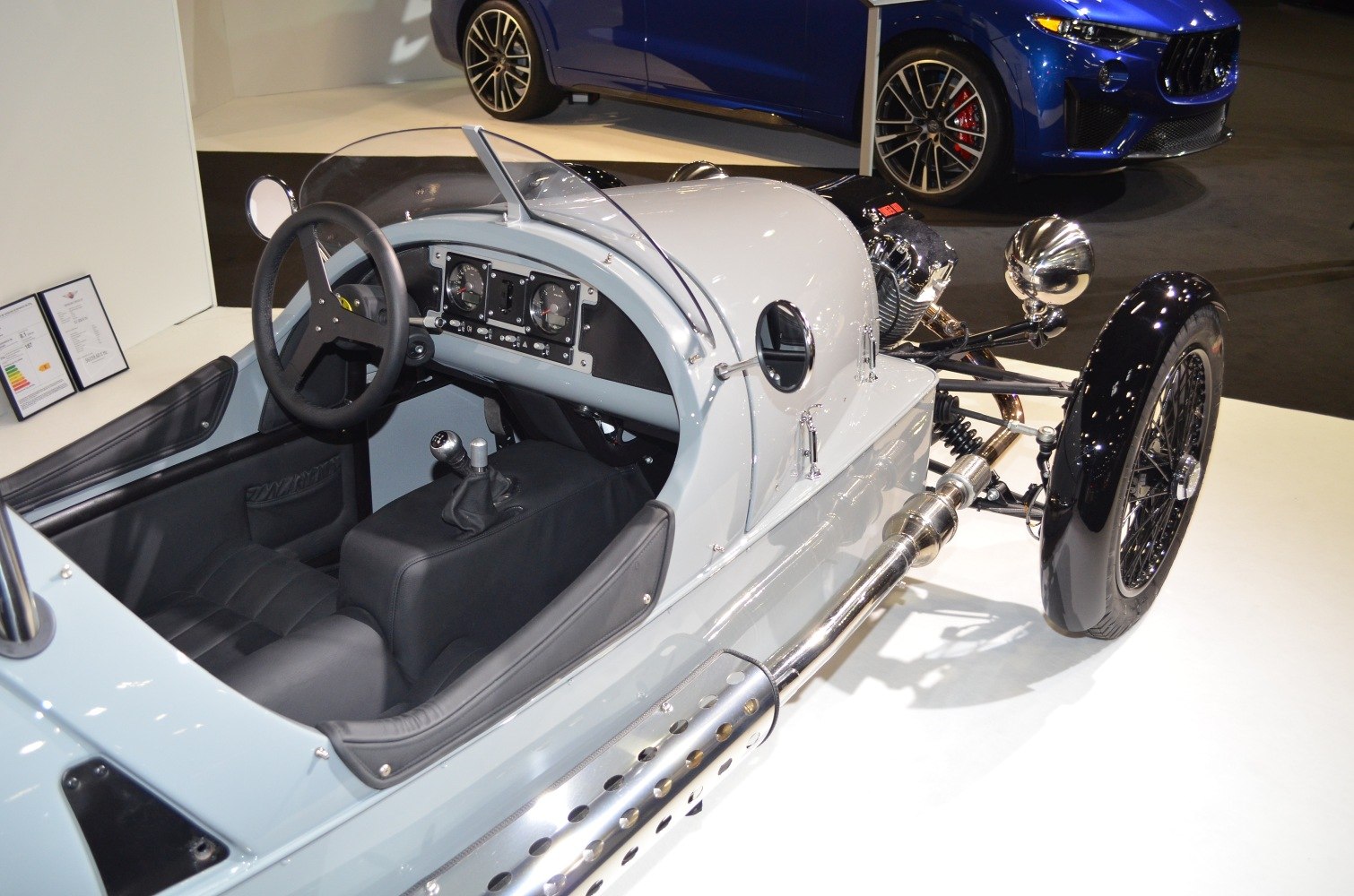 Open cabin with manual gearbox and exposed engine on a three-wheeled roadster.
