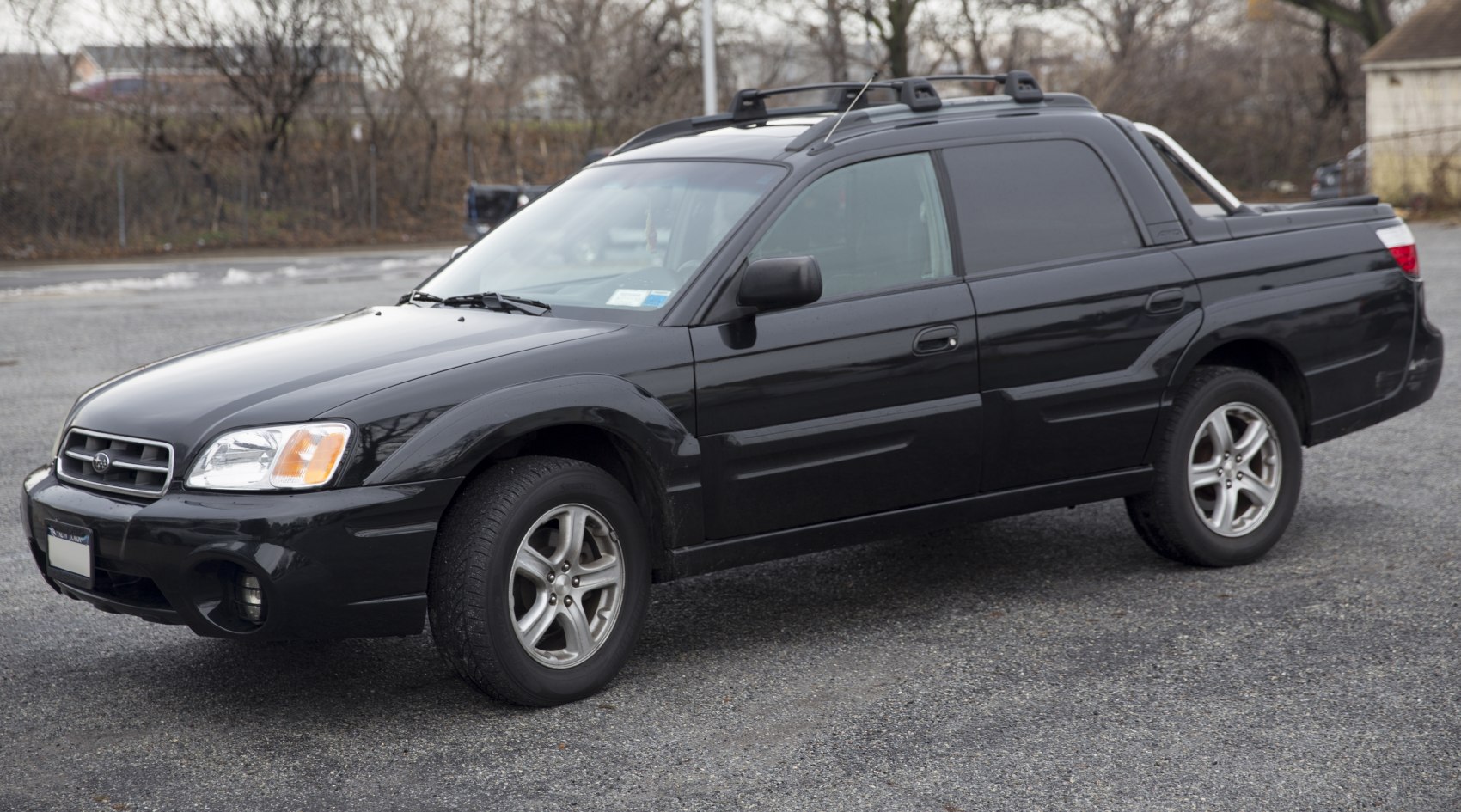 Black pickup truck with roof rack and rugged tires on gravel surface