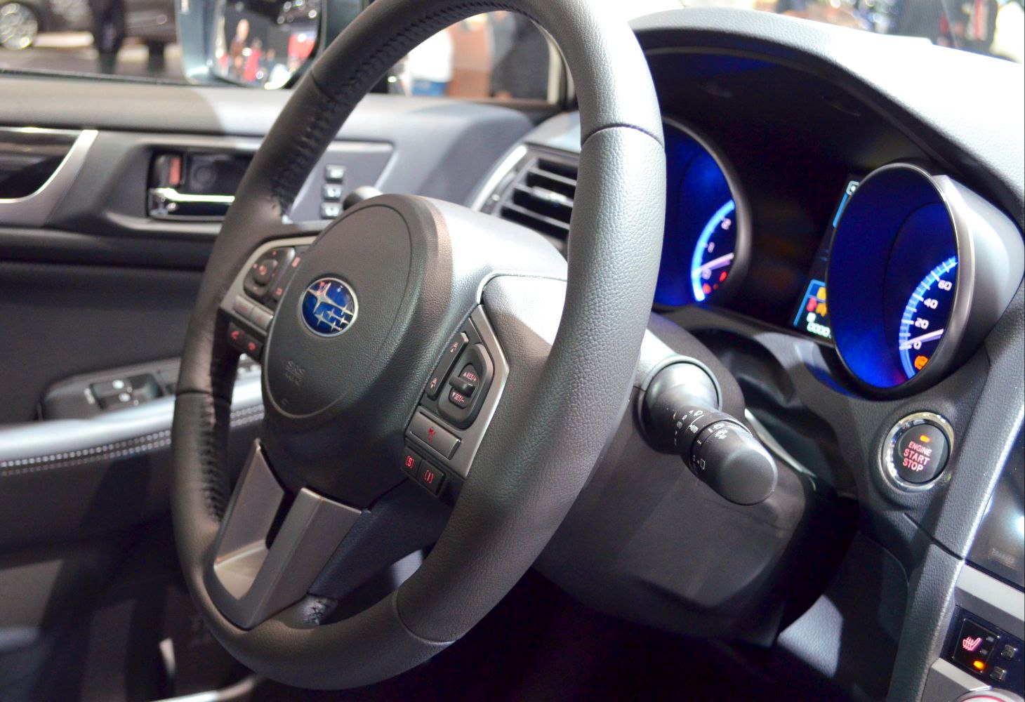 Steering wheel with control buttons and illuminated blue instrument cluster.