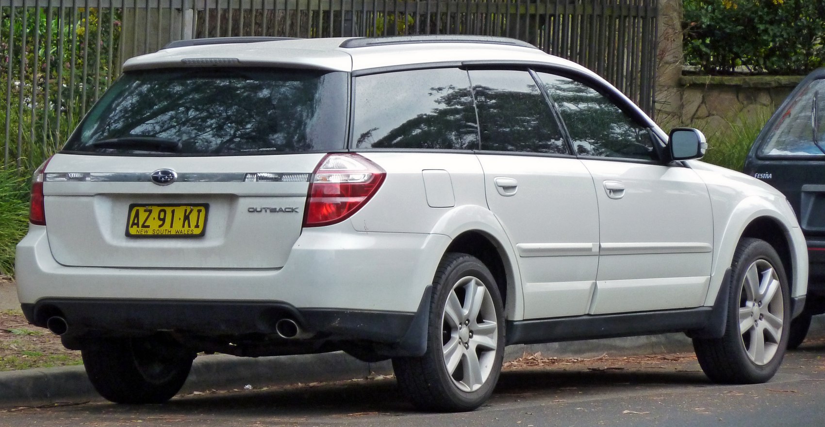 Rear side view with station wagon body and dual exhaust of white vehicle.