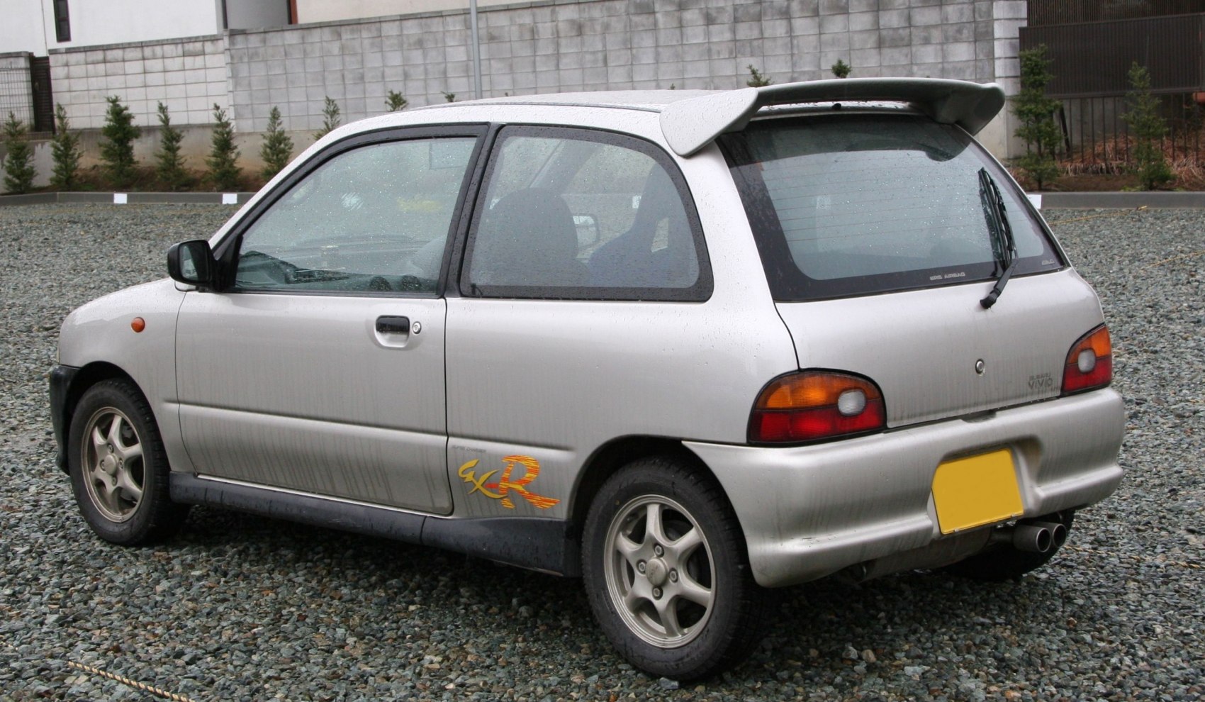 Rear side view of a compact hatchback with rear spoiler and dual exhaust
