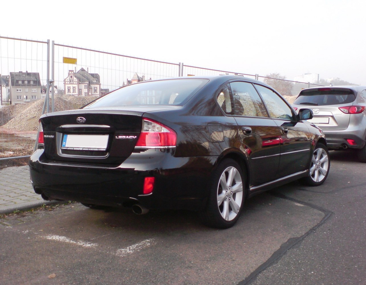 Rear and side view of black sedan with taillights and dual exhausts.