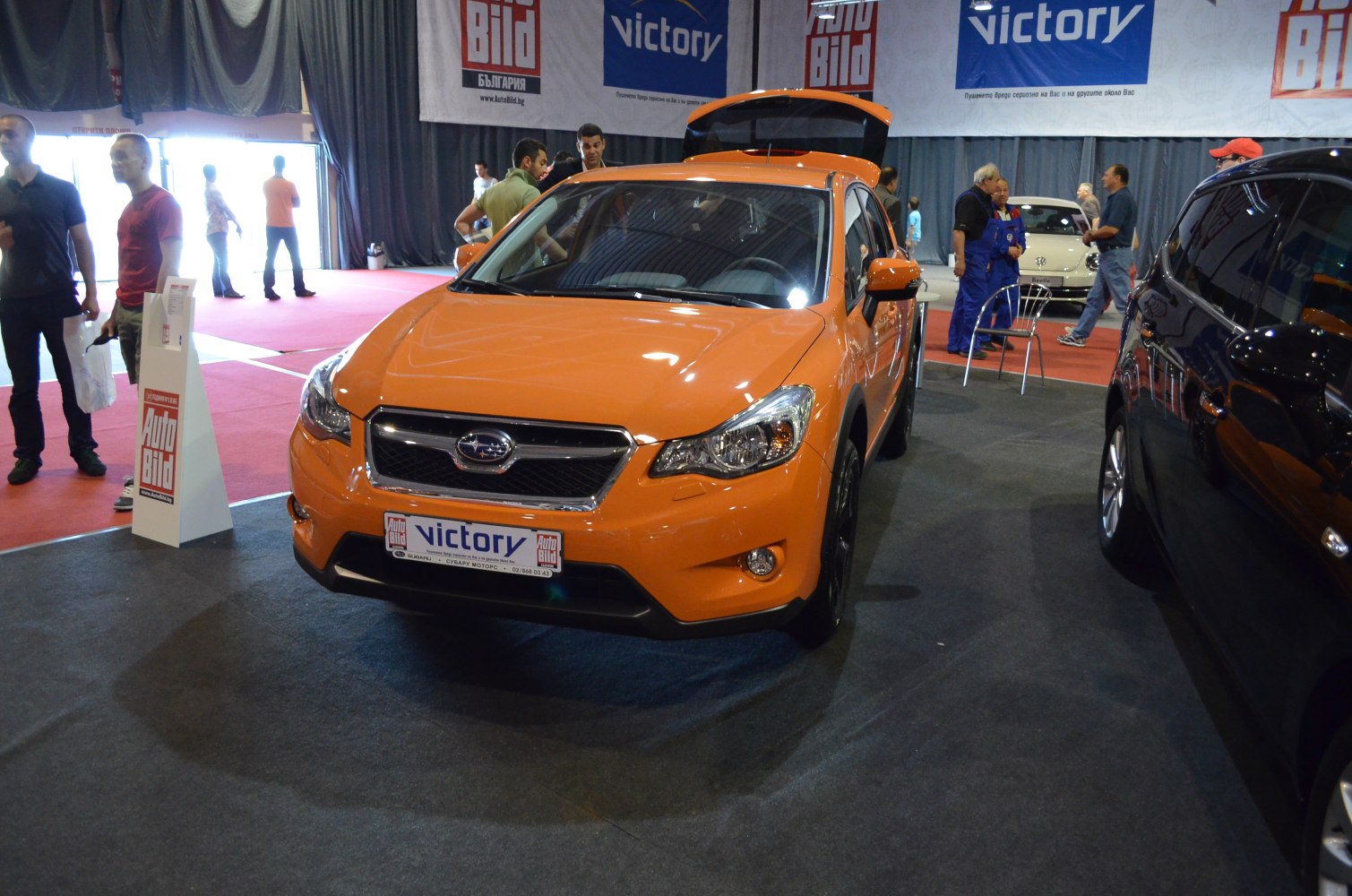 Orange compact SUV front with open trunk at indoor show