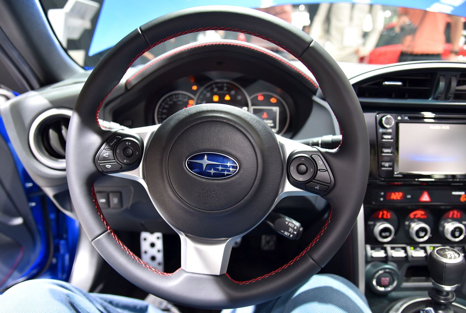 Leather-wrapped steering wheel with red stitching and dashboard controls