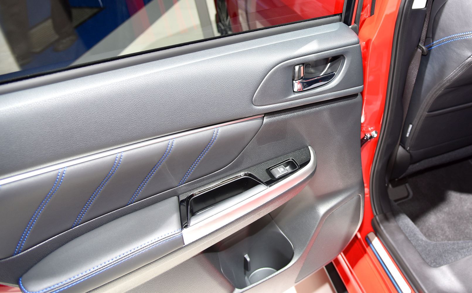 Rear door interior panel with blue stitching and ergonomic handle.