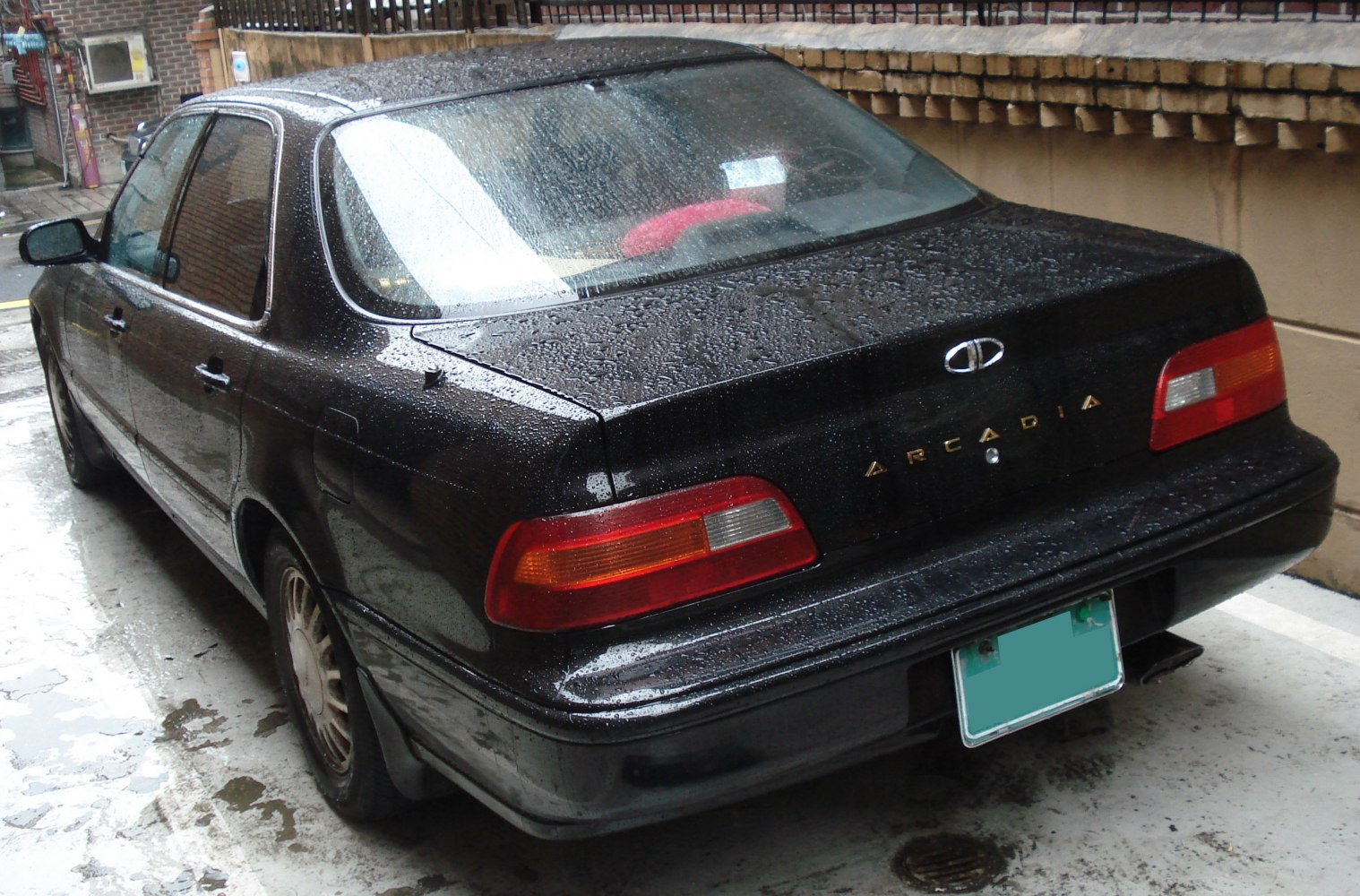 Rear view of a mid-size sedan with wide tail lights and wet surface