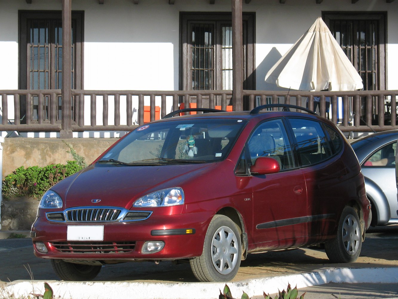 Red compact MPV showing front-side view with distinctive grille and roof rails