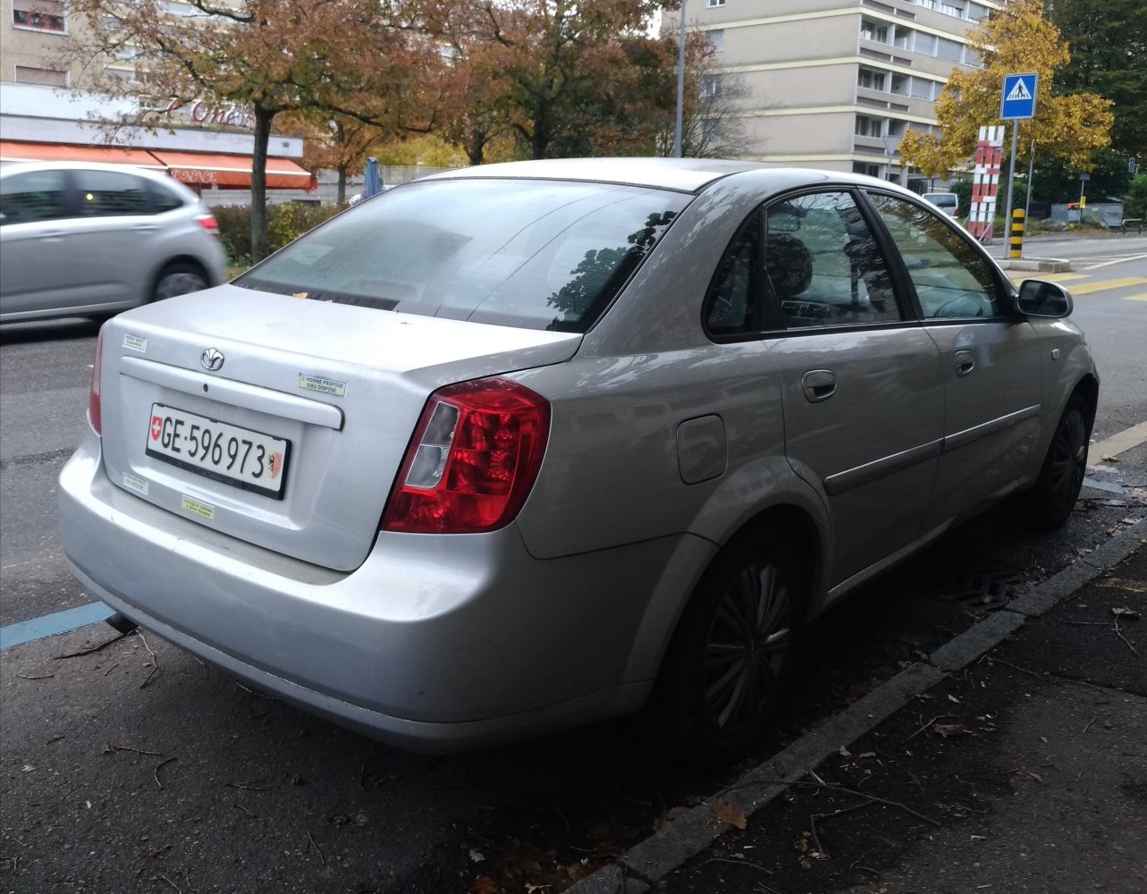 Silver sedan rear and side view with red taillights parked on street