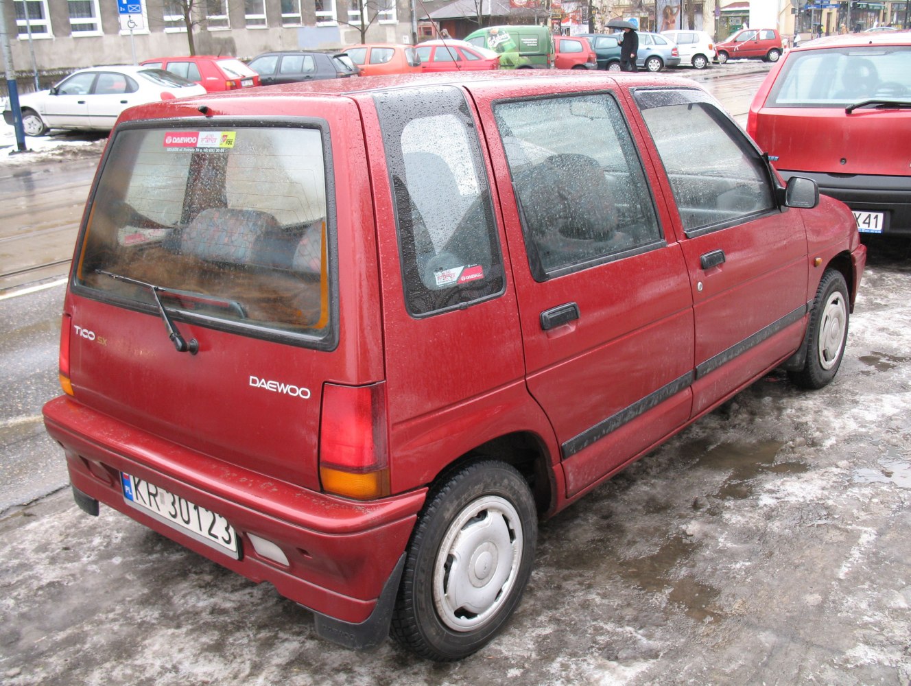 Rear and side view of red compact hatchback with rear wiper on wet pavement.