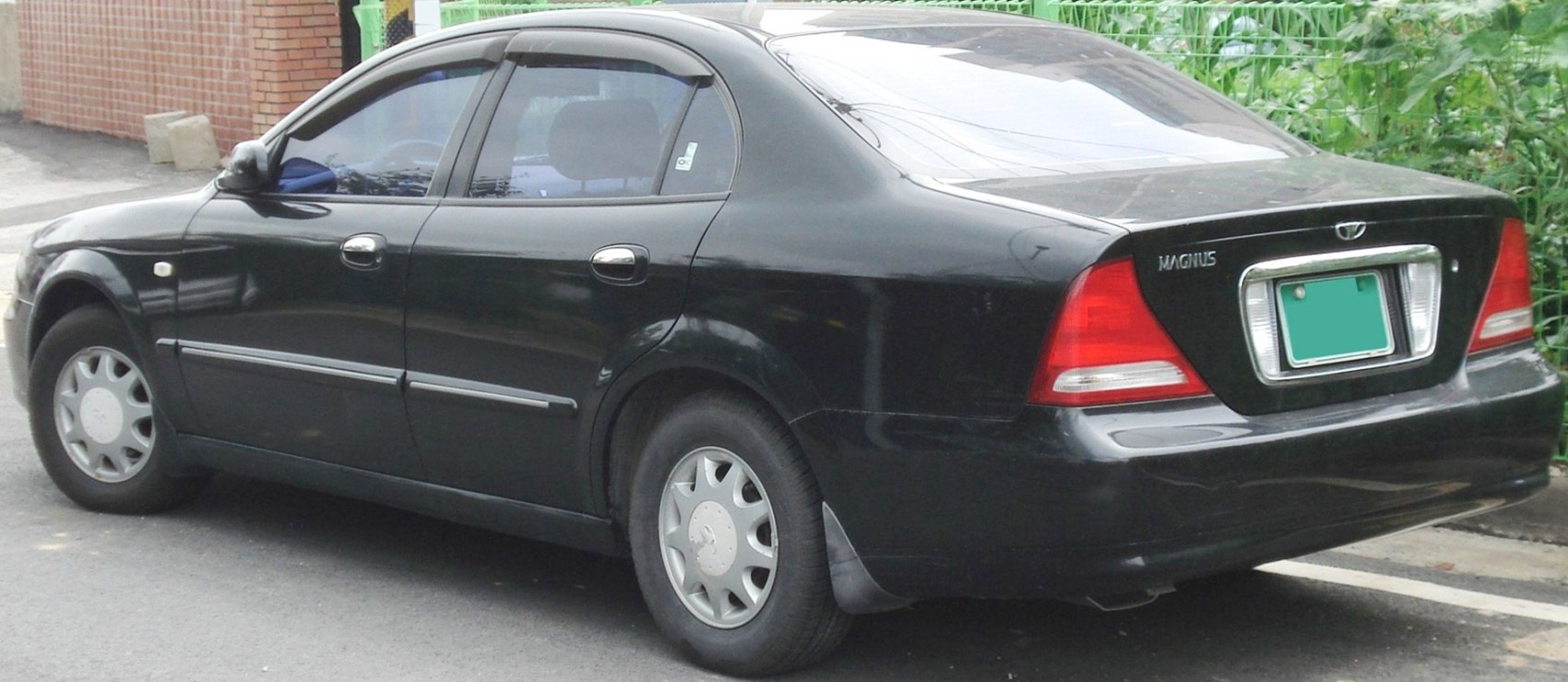 Rear side view of a black sedan with hubcaps and rear lights.