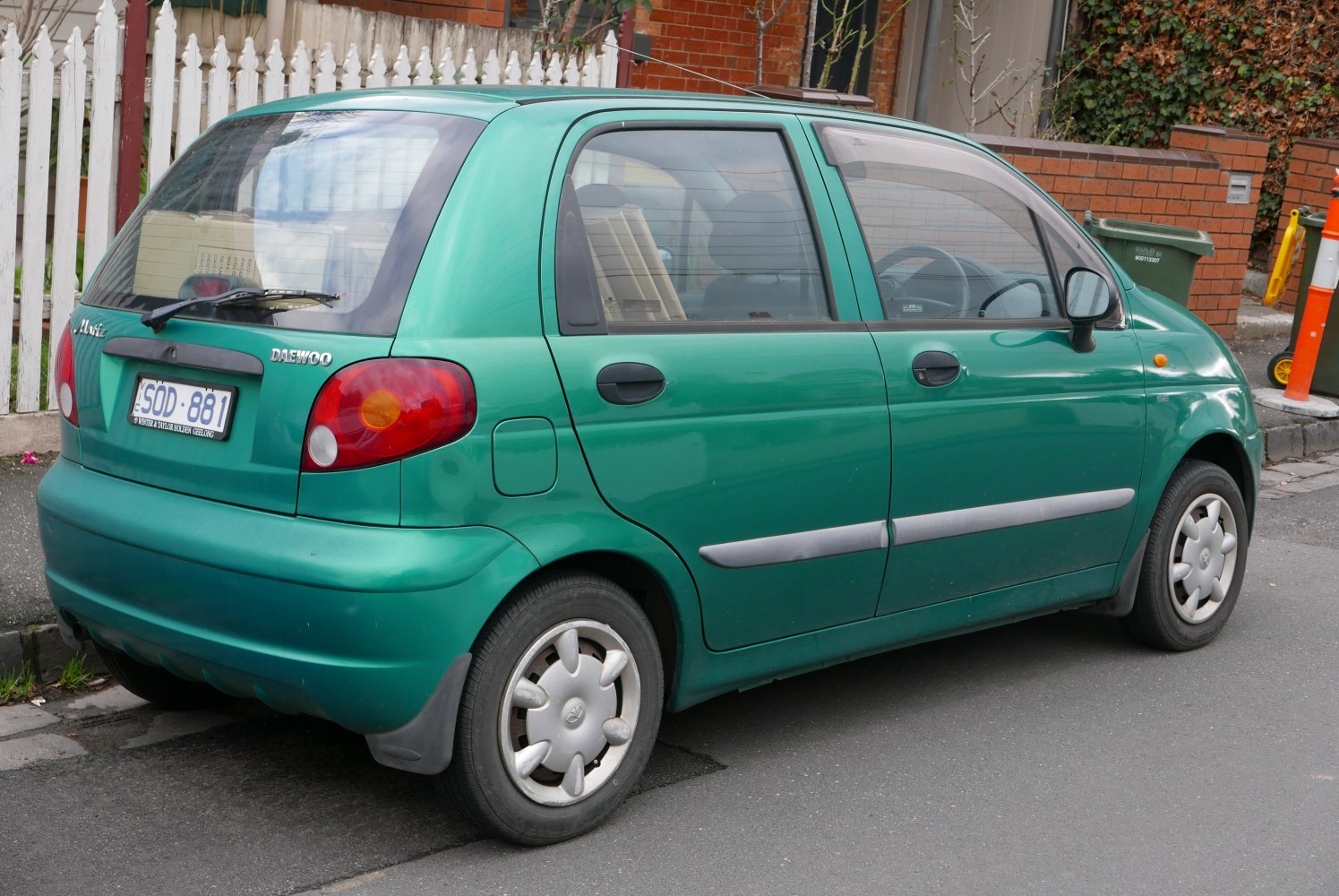 Compact green hatchback rear side with rounded tail lights and black door handles.