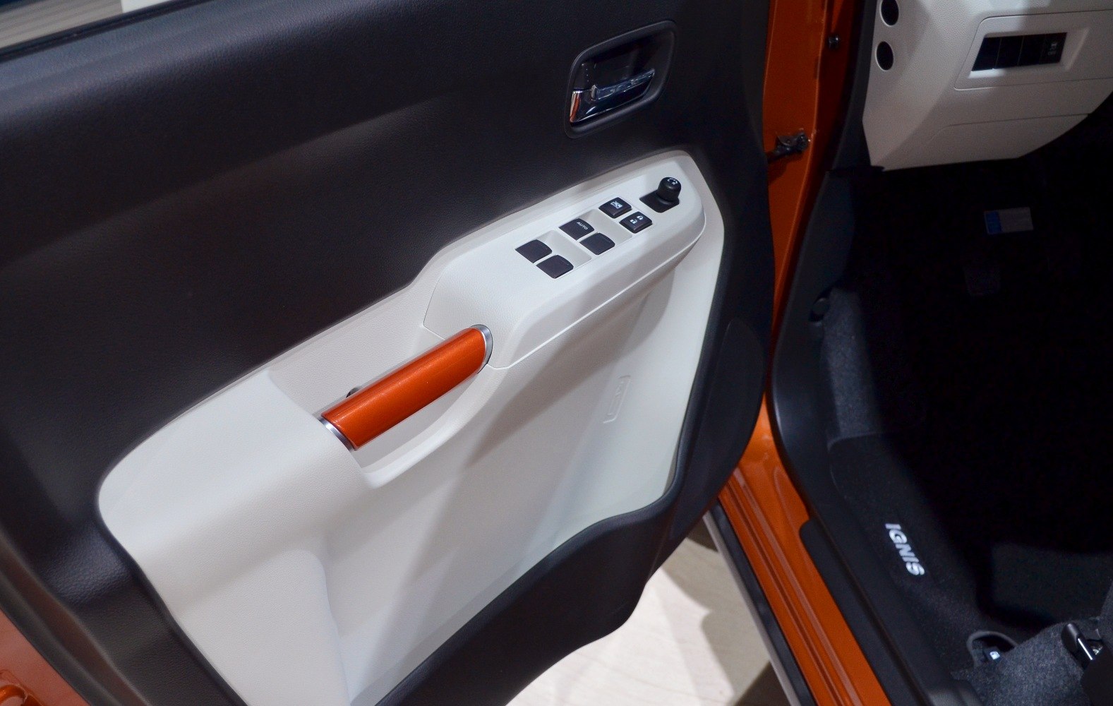 Car interior door panel with window control buttons and orange handle.