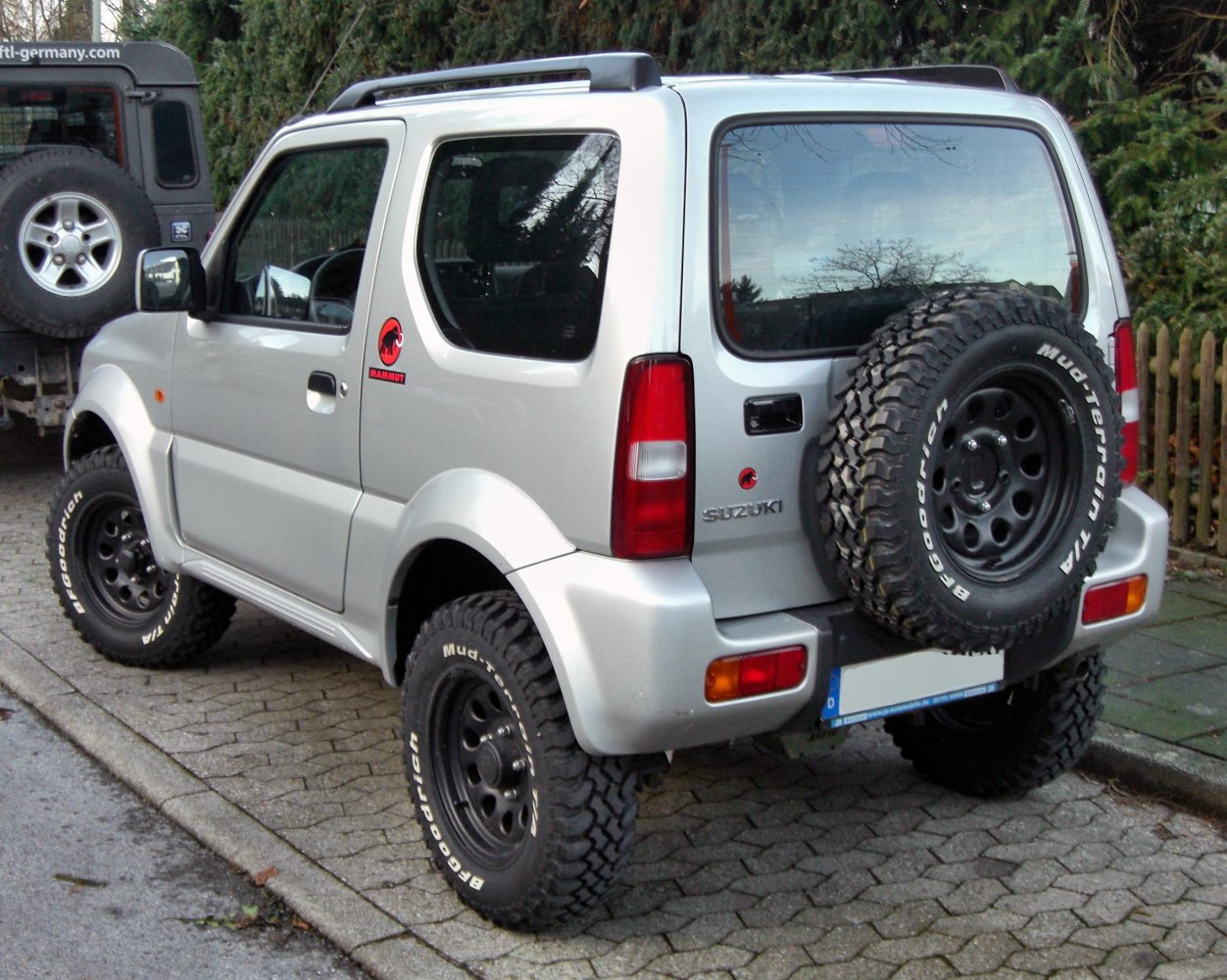 Rear side view showing compact SUV with off-road tires and rear-mounted spare wheel.
