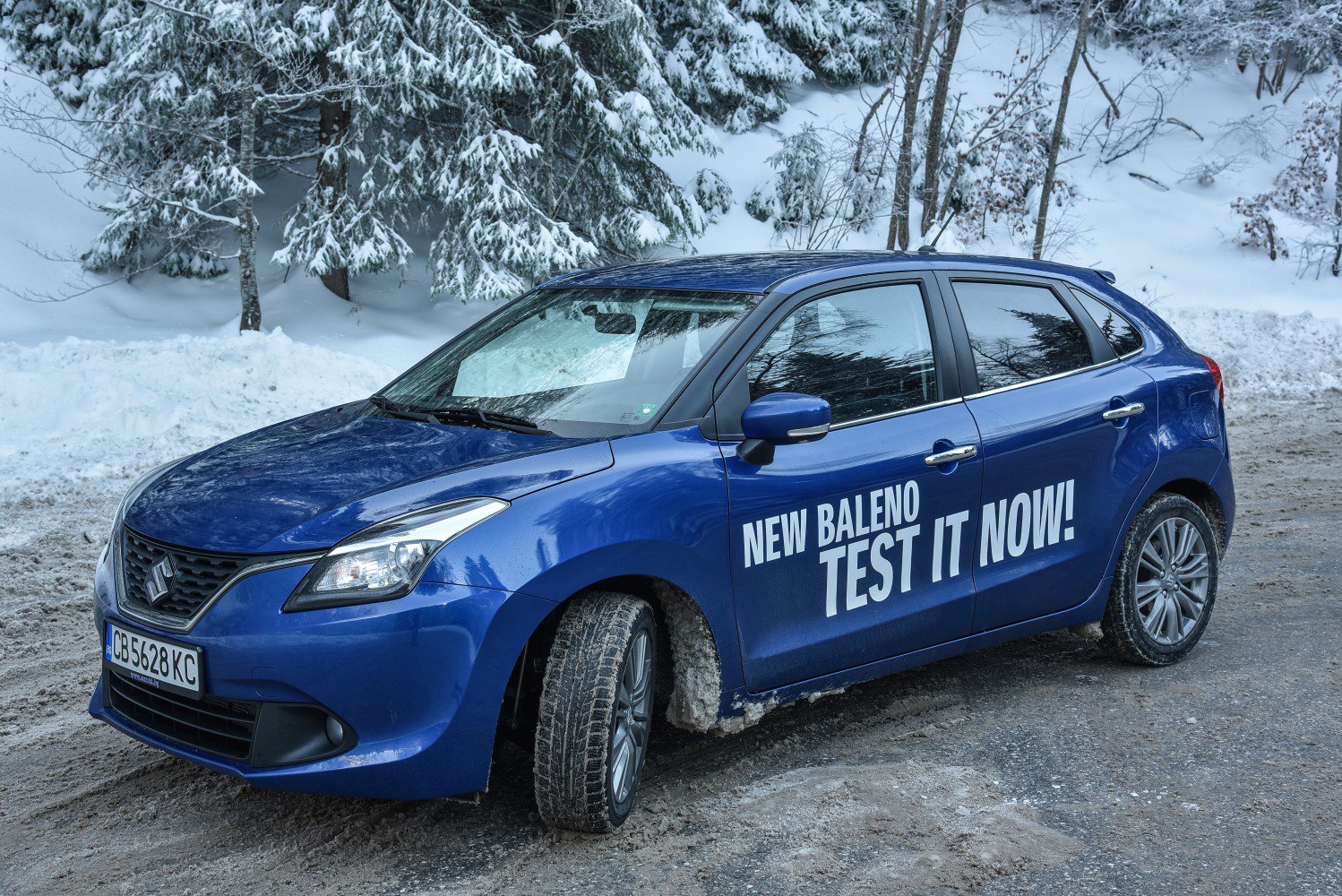 Blue hatchback with test drive text on door in snowy forest setting