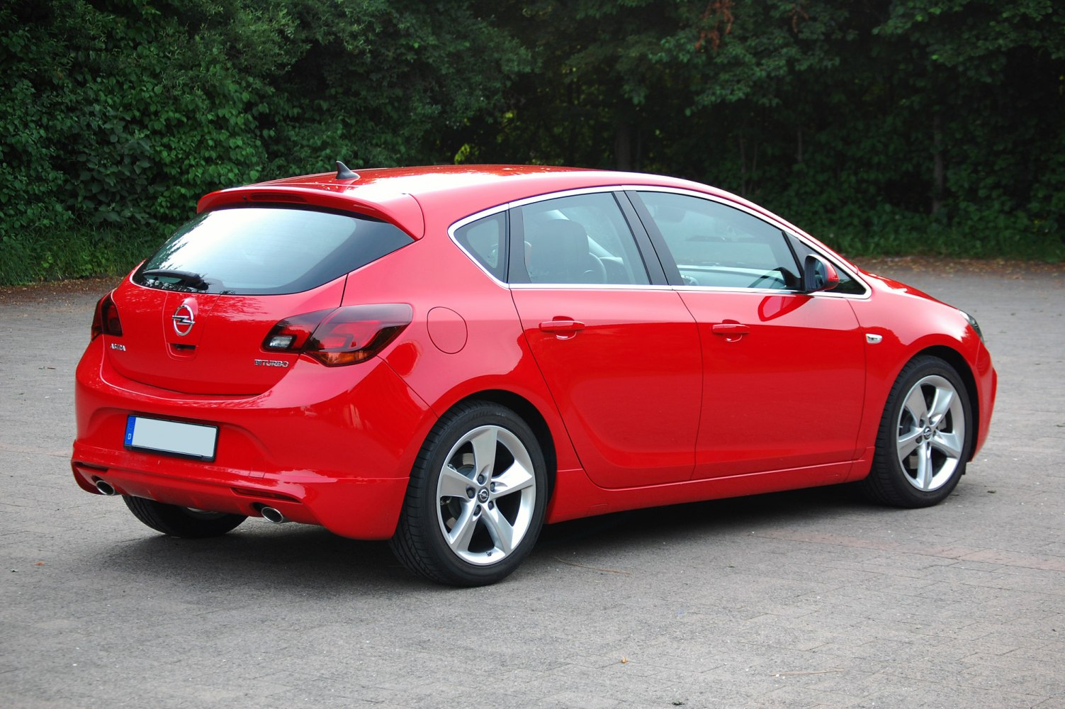 Red hatchback rear side view with alloy wheels and dual exhaust