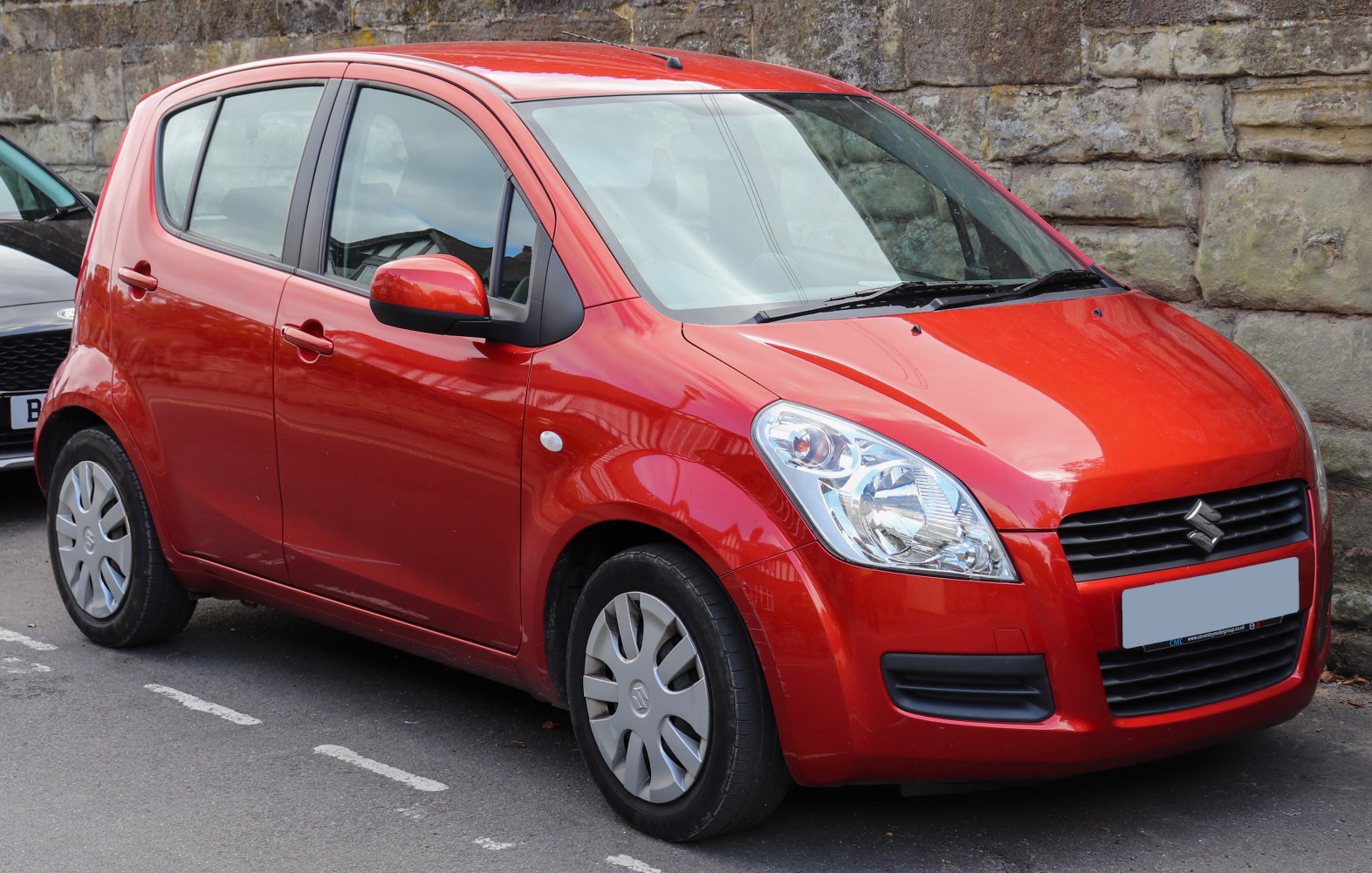 Compact red five-door hatchback with large headlights and black grille