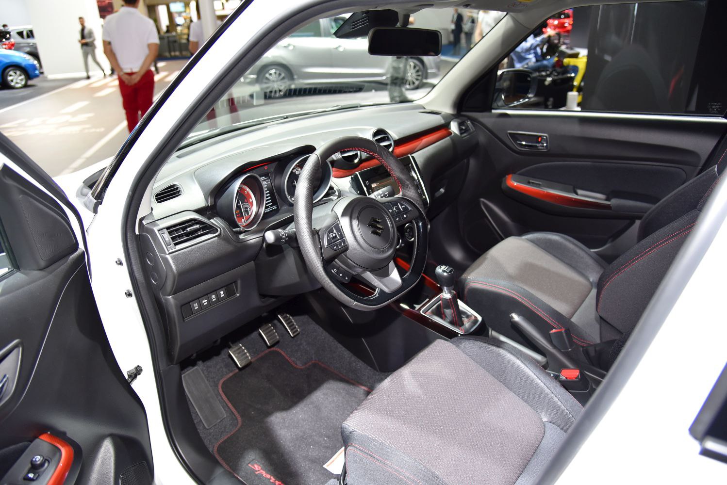 Sporty steering wheel and manual transmission interior with detailed dashboard and red stitching.