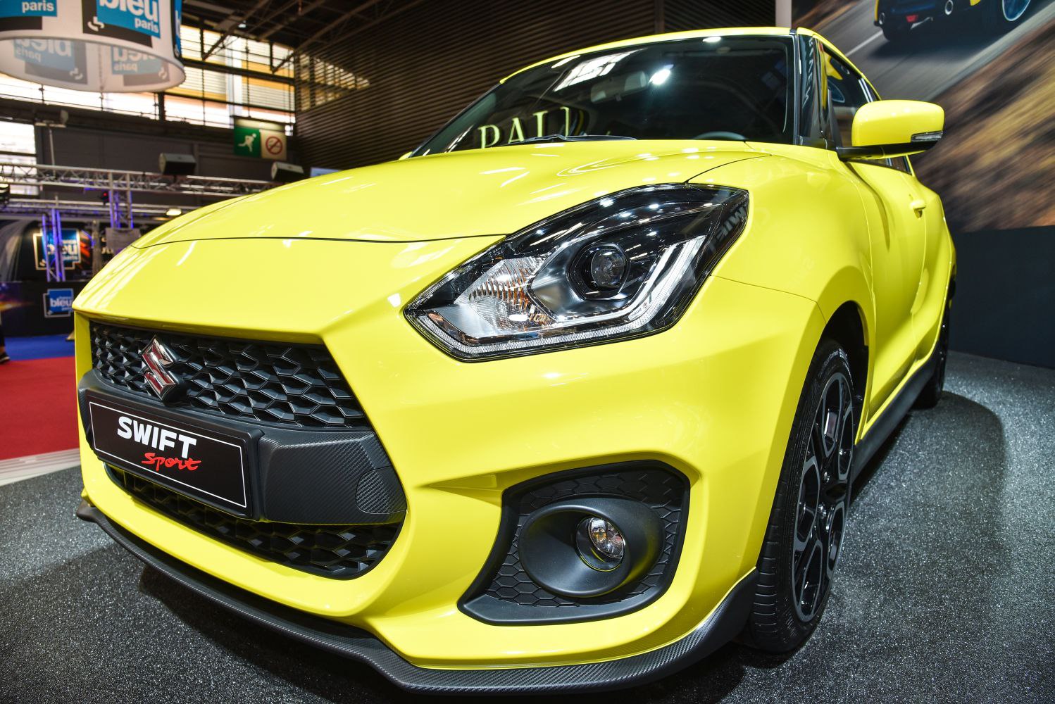 Close-up of a yellow car's front grille with headlights and fog light.