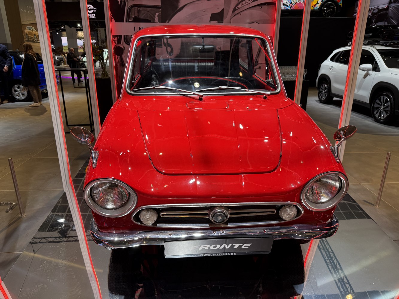 Classic compact car front with round headlights and chrome bumper.