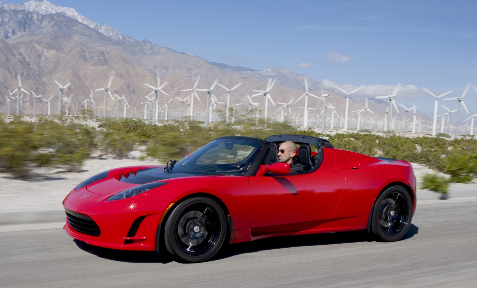 Red convertible sports car driving with desert and wind turbines background