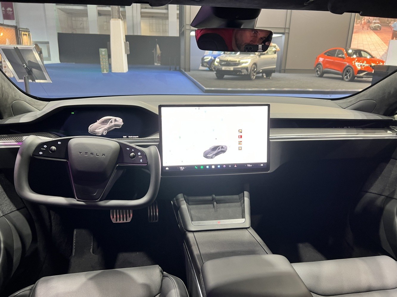Yoke steering wheel and large central touchscreen display in modern electric car interior.
