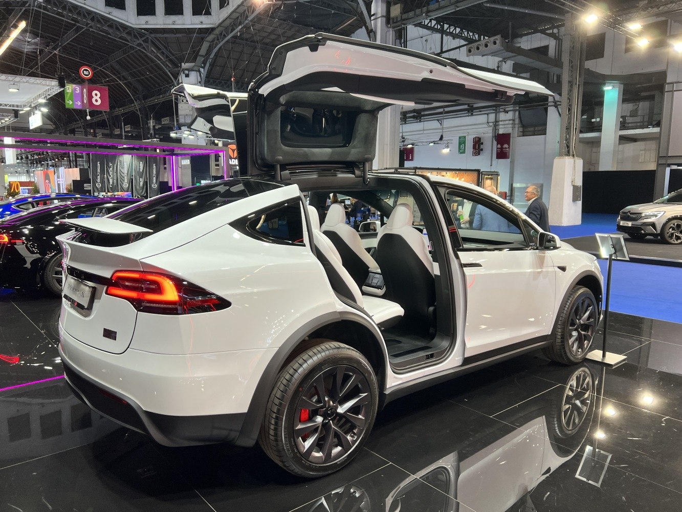 White electric SUV with prominent falcon wing doors open.