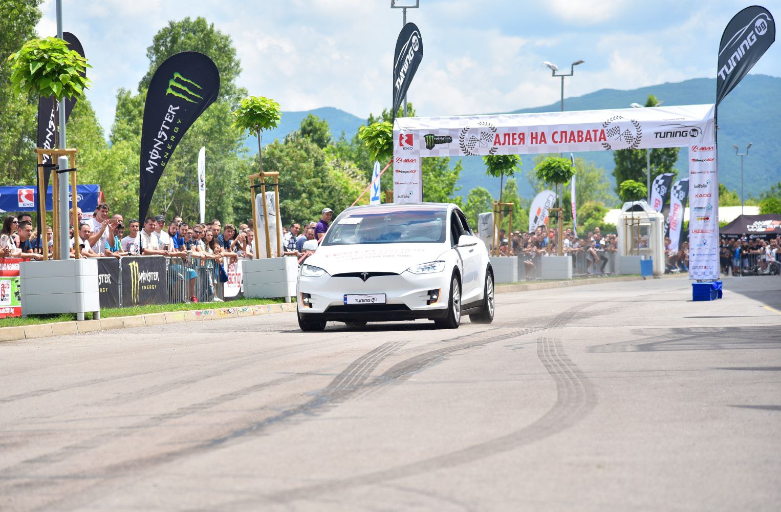 White electric SUV racing amidst crowds and banners