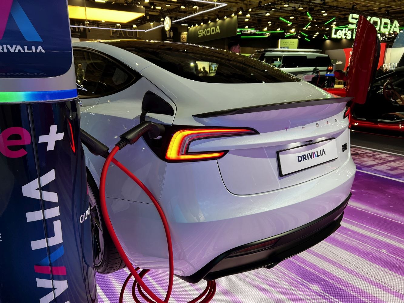 Rear view of electric vehicle plugged into charging station with illuminated taillights