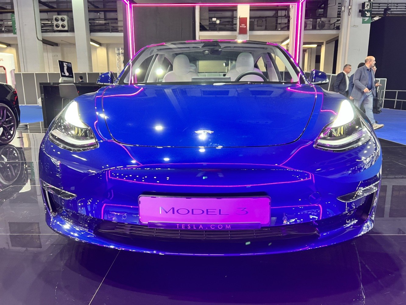 Front view of blue Tesla Model 3 facelift with headlights on