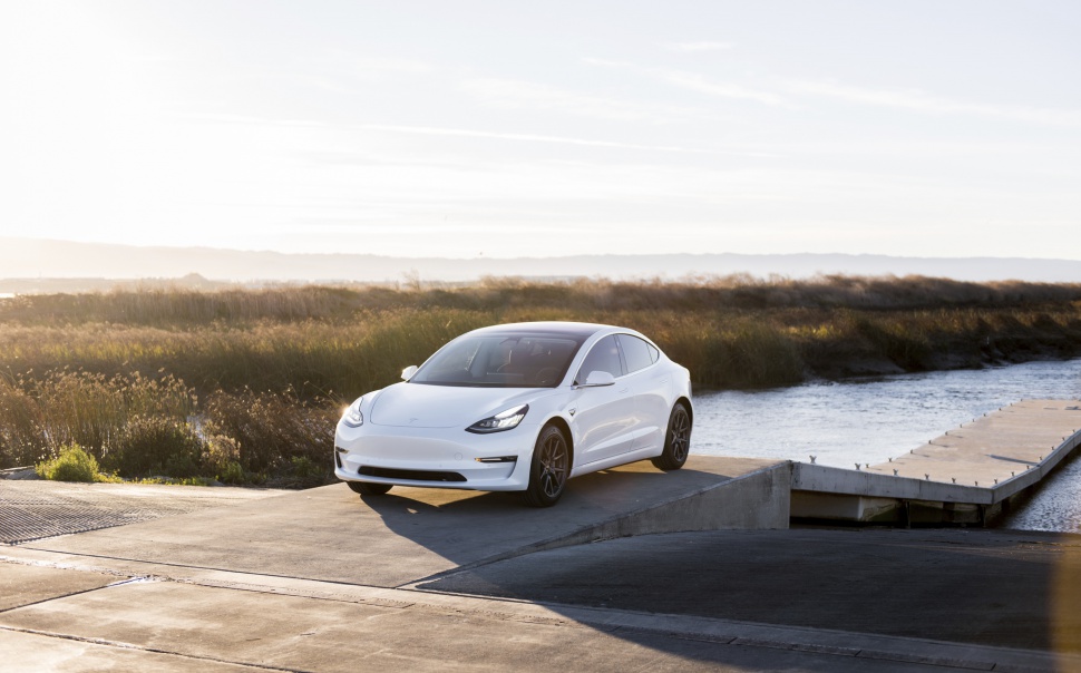 Sleek electric sedan with LED headlights near waterfront in natural daylight.
