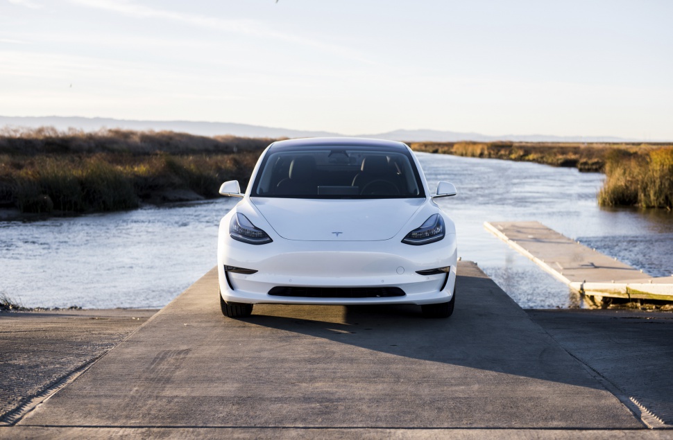 Front view of electric sedan with sleek headlights on concrete near waterway