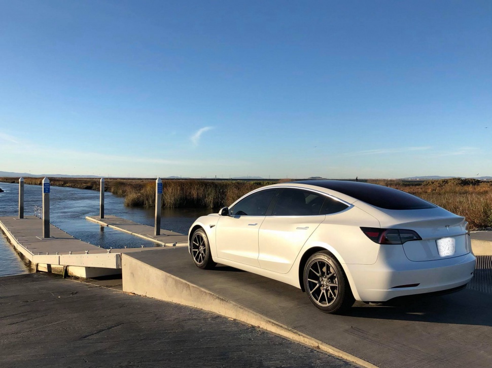 White electric sedan rear parked near dock waterside