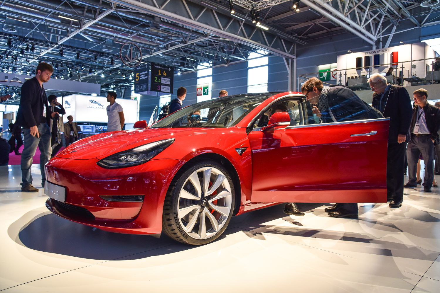Red electric sedan with open front door and alloy wheels