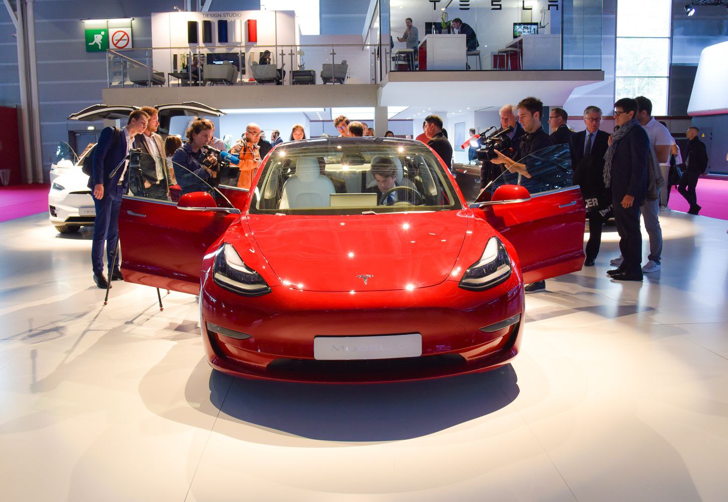 Front view of a red electric sedan with open doors at an auto show