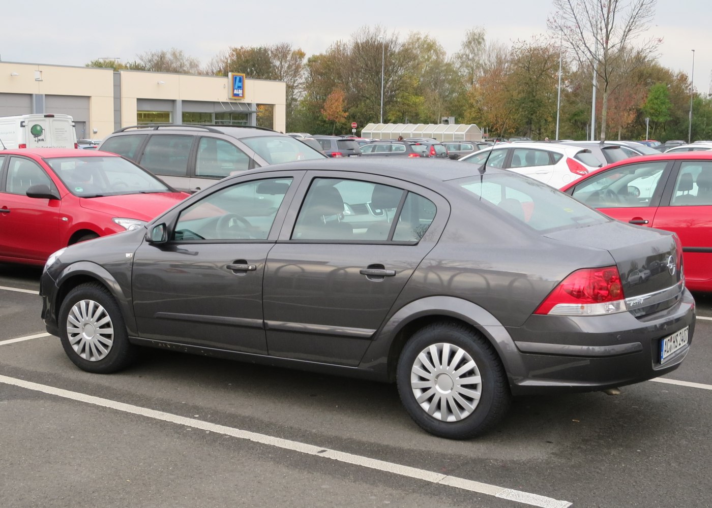 Side profile of a dark gray compact sedan with hubcap wheels parked in an open lot