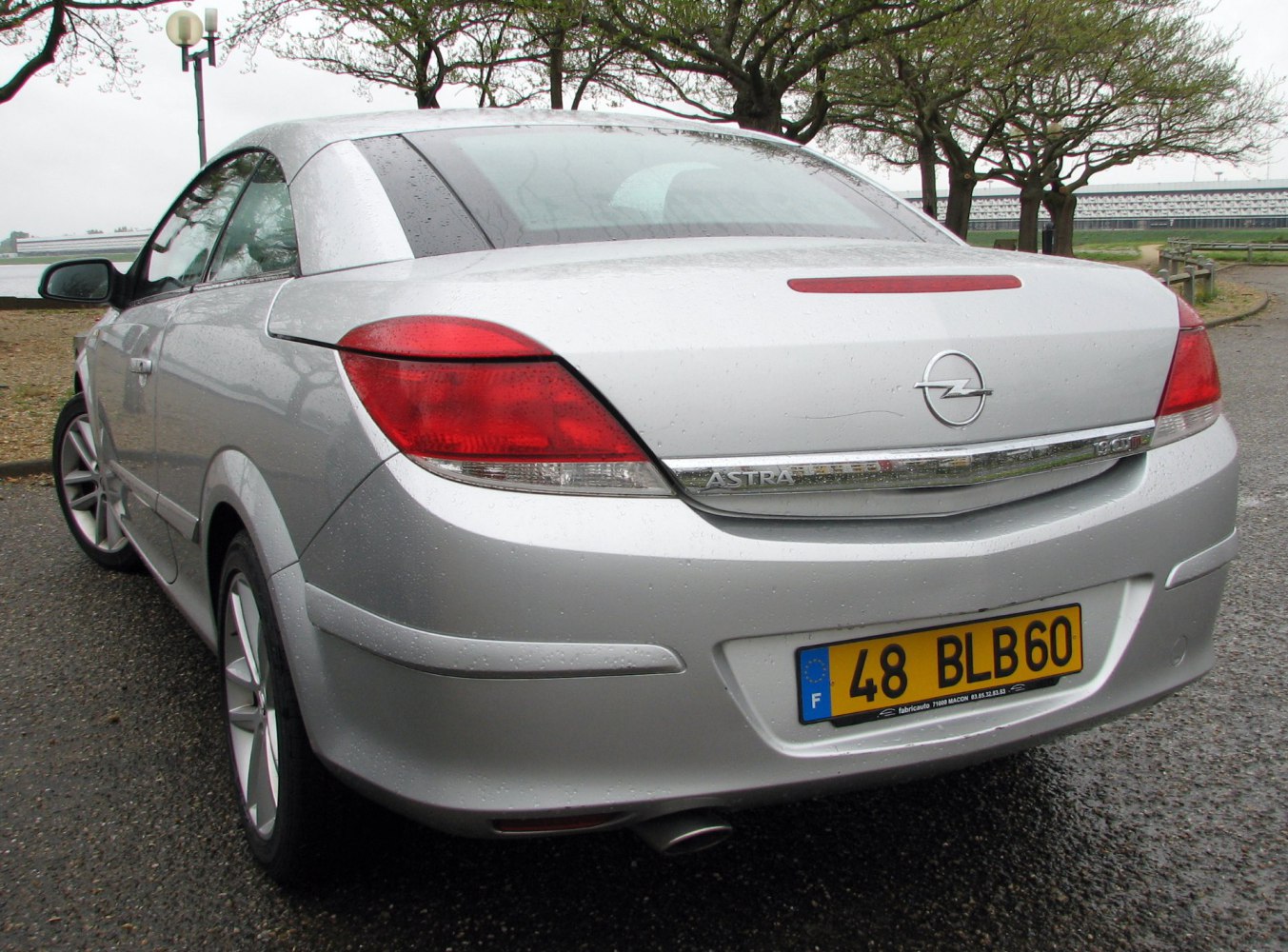Rear profile of a silver convertible coupe with prominent taillights and exhaust pipe.