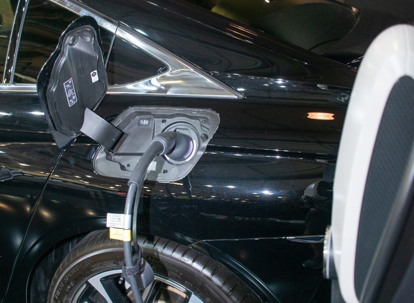 Electric vehicle charging port on rear side panel with charging cable connected.