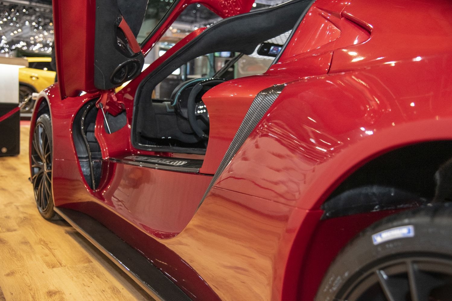 Red sports coupe side with carbon trim and vertical scissor door