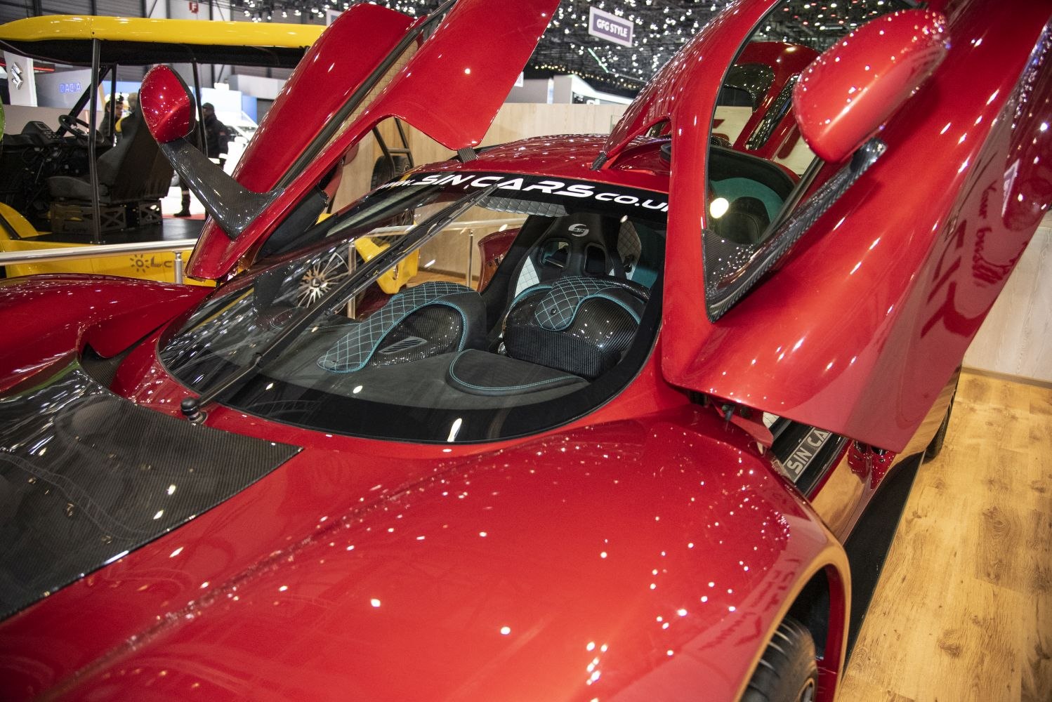 Red sports car with gullwing doors and carbon fiber interior with blue stitching.