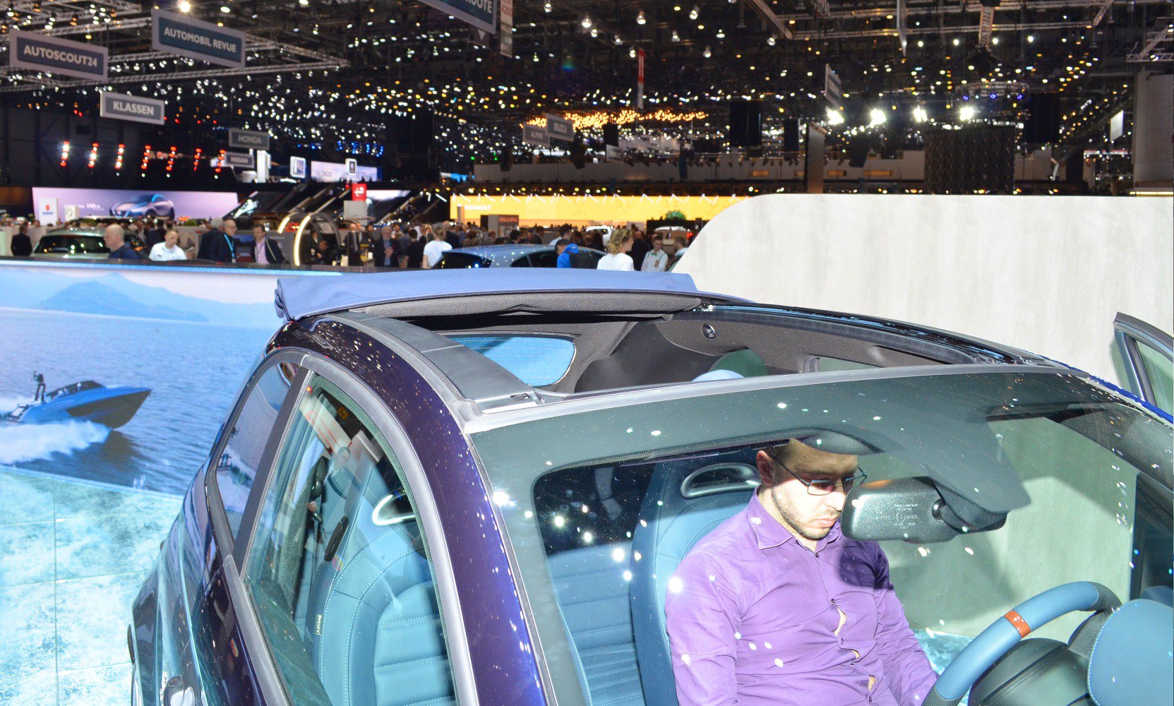 Convertible roof and blue interior visible with driver at an auto show.