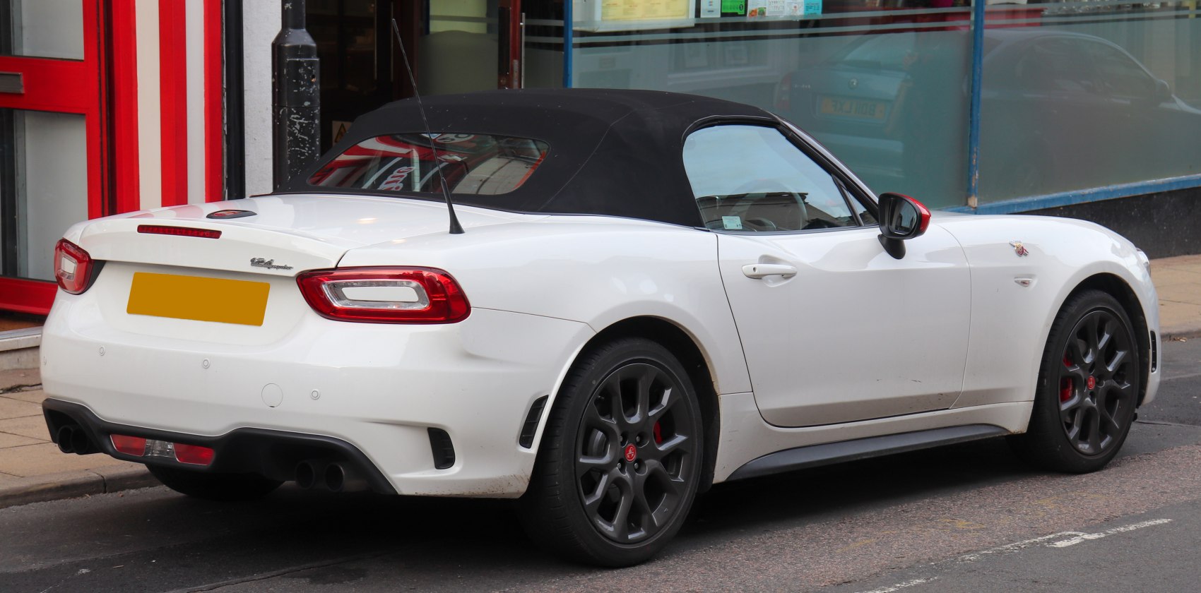 Rear side view of a white convertible roadster with black soft top and sporty wheels