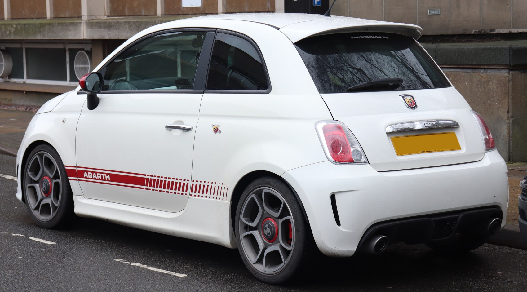 Rear side view of sporty white hatchback with red stripes and dual exhaust