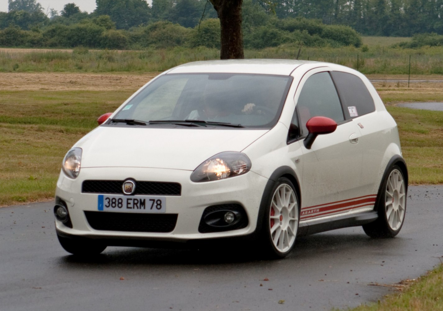 White compact hatchback with red mirror caps, sporty side stripes, and white alloy wheels