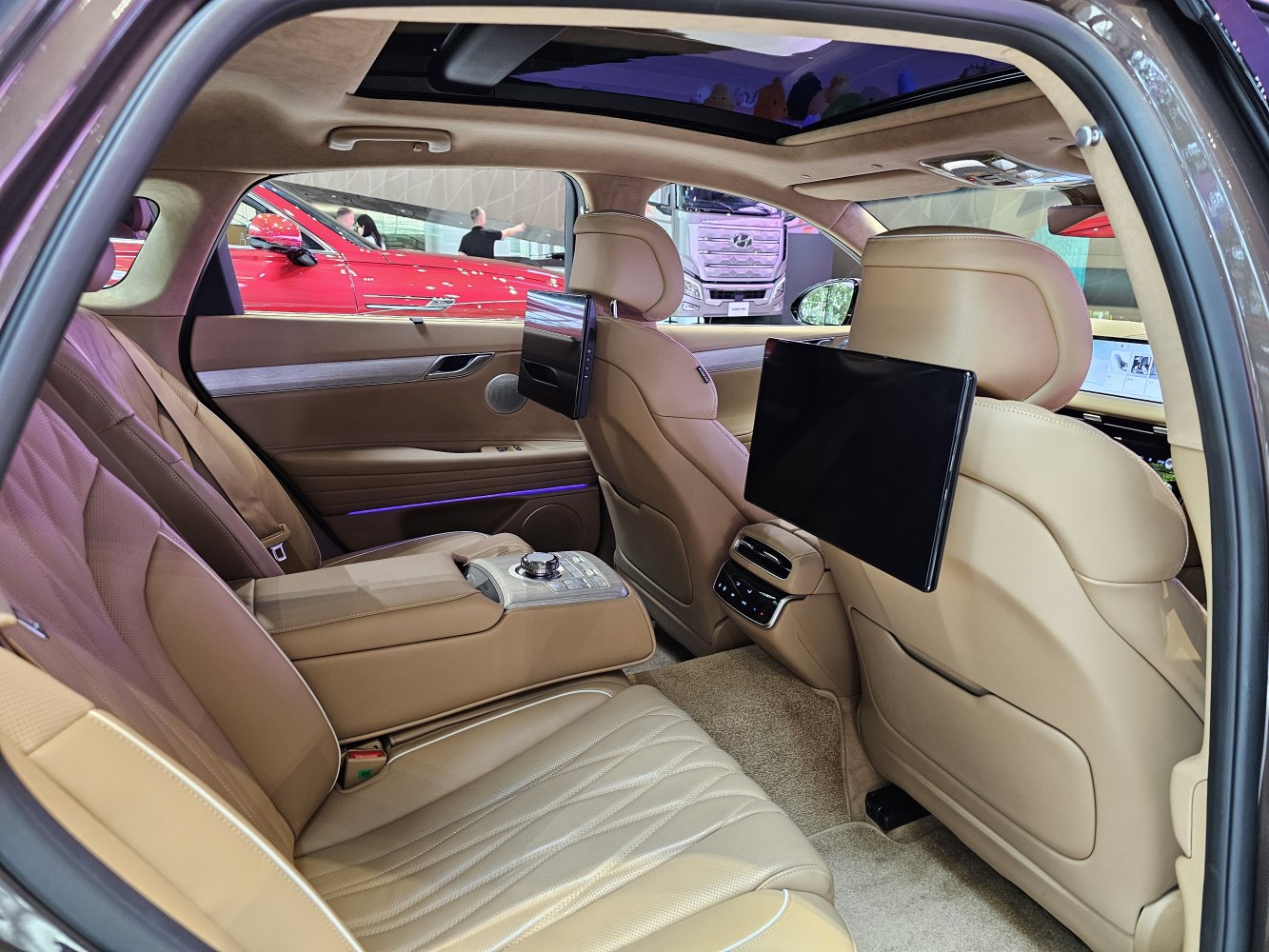 Rear cabin with beige leather seats, dual screens, armrest controls, and sunroof