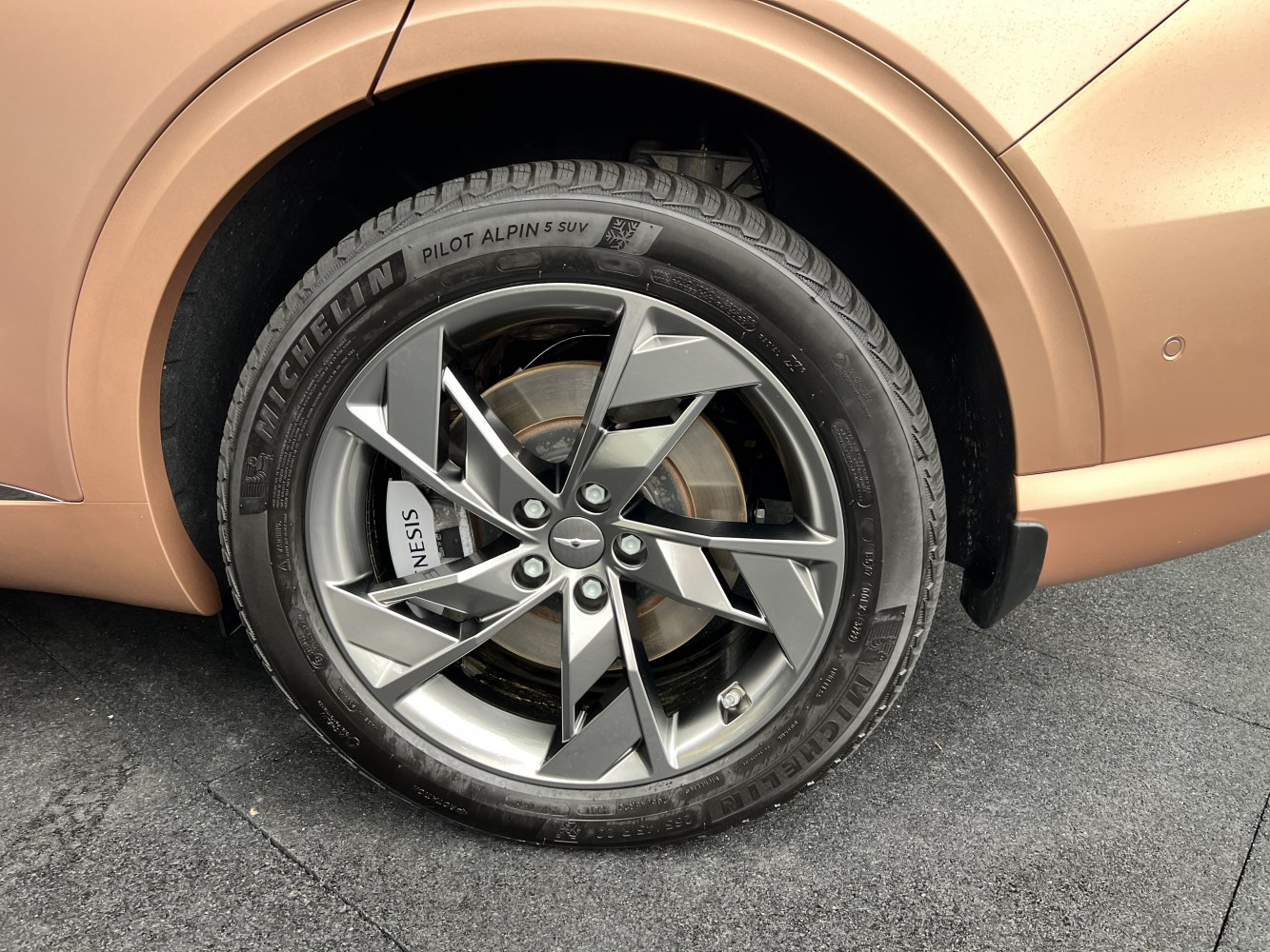 Alloy wheel with Michelin Pilot Alpin 5 SUV tire on medium brown vehicle.