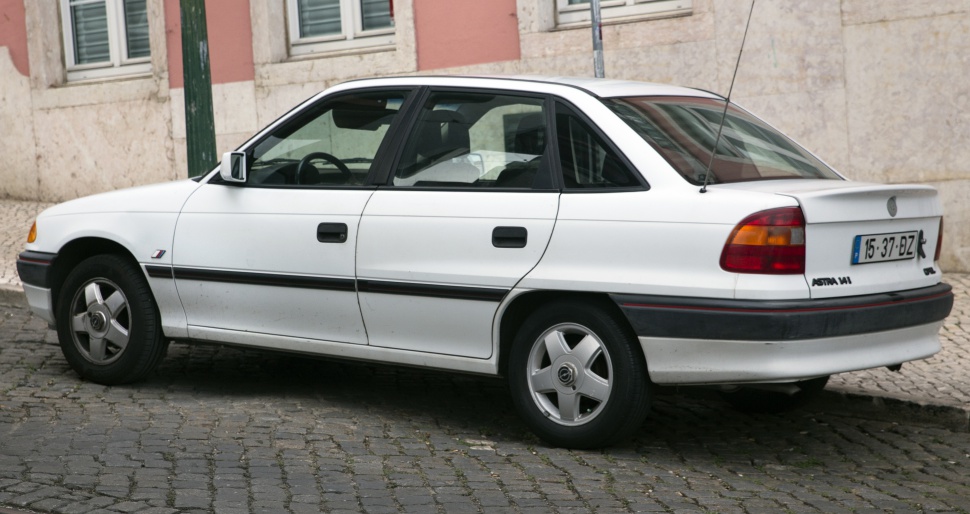 White mid-1990s four-door sedan with rear spoiler and roof antenna.