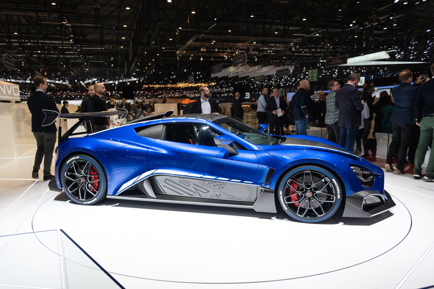 Blue sports car with large rear wing and aerodynamic carbon fiber accents.