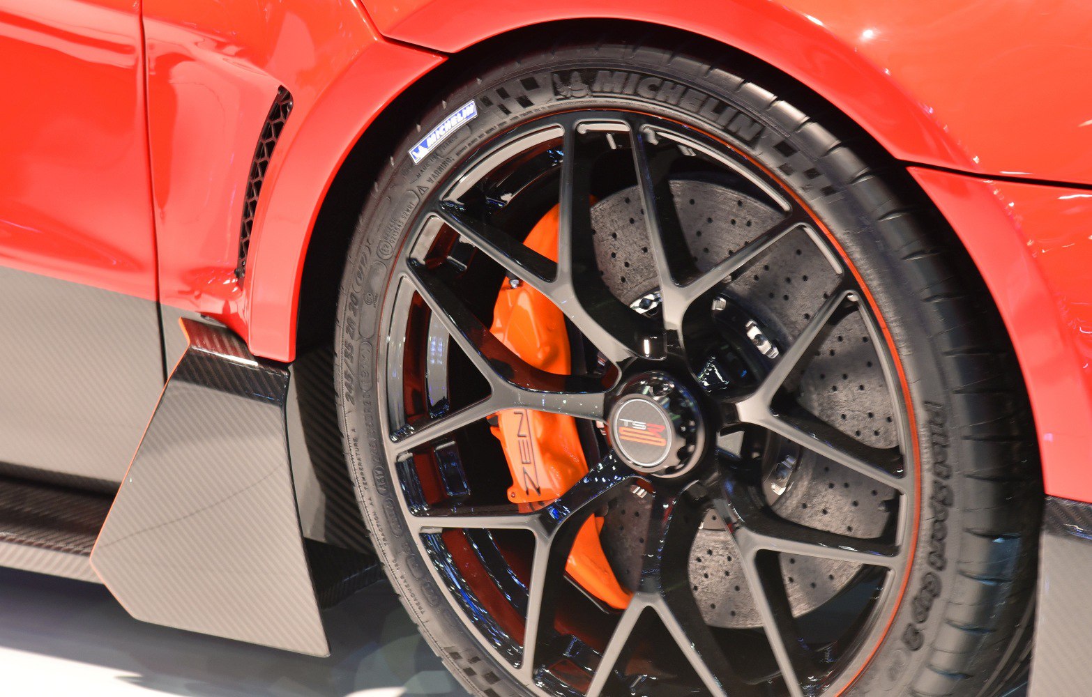 Black alloy wheel with orange brake caliper and carbon fiber detail